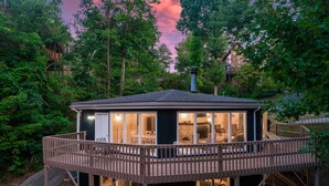 A wooden decked structure with a glass enclosure, surrounded by trees. - Stylish Modern 6 Bdrm + Hot Tub + Pool Access (Gatlinburg)