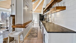 A modern kitchen with white cabinetry, wooden beams, and a granite countertop. - Stylish Modern 6 Bdrm + Hot Tub + Pool Access (Gatlinburg)