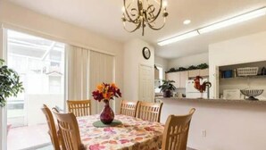 A dining area with a floral tablecloth, wooden chairs, a vase with flowers, and a chandelier. - 💖20 mins 2 Disney; 400Mbps WiFi; 2 Masters✔️Gated (Kissimmee)
