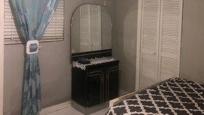 A bedroom with a bed, a dresser, a mirror, an air conditioning unit, and a closet. - Comfort Breeze Studio (Nassau)