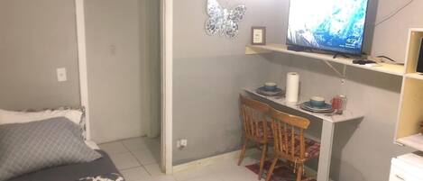 A small, compact room with a bed, a desk with a chair, a television, and a small refrigerator.