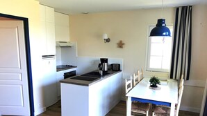 Een compacte keuken met een centraal eiland, een eettafel met stoelen en een hangende lamp.