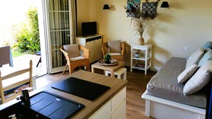 Een gezellig, compact verblijf met een kitchenette, een bank, twee fauteuils, een klein tafeltje en een televisie op een kast.
