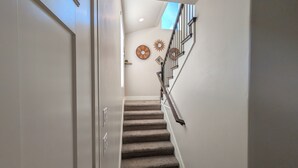 A staircase with a handrail, carpeted steps, and a wall with a decorative sunburst mirror and a small framed picture. - Modern 3BR Hildale Oasis near Zion, King Bed & Balcony, Massive Cliff Views! (Hildale)
