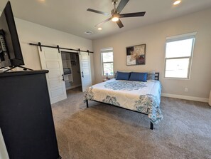 Une chambre à coucher avec un lit, un ventilateur de plafond, une télévision, un placard et une fenêtre.
