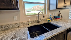 A kitchen with a granite countertop, stainless steel sink, and a window with a view of a building and trees. - Modern 3BR Hildale Oasis near Zion, King Bed & Balcony, Massive Cliff Views! (Hildale)