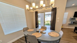 A dining area with a round table, six chairs, woven placemats, and a chandelier. - Modern 3BR Hildale Oasis near Zion, King Bed & Balcony, Massive Cliff Views! (Hildale)