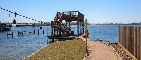 Une terrasse au bord de l’eau, avec un escalier en bois menant à une plateforme, le tout entouré d’un chemin de gravier et d’une clôture en bois.