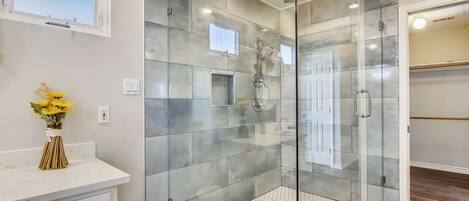 Un baño moderno con ducha separada por vidrio, tocador blanco y una ventana pequeña.