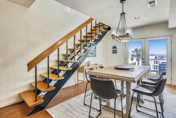 A modern interior with a wooden staircase, a dining area with a table and chairs, and a view through a glass door.