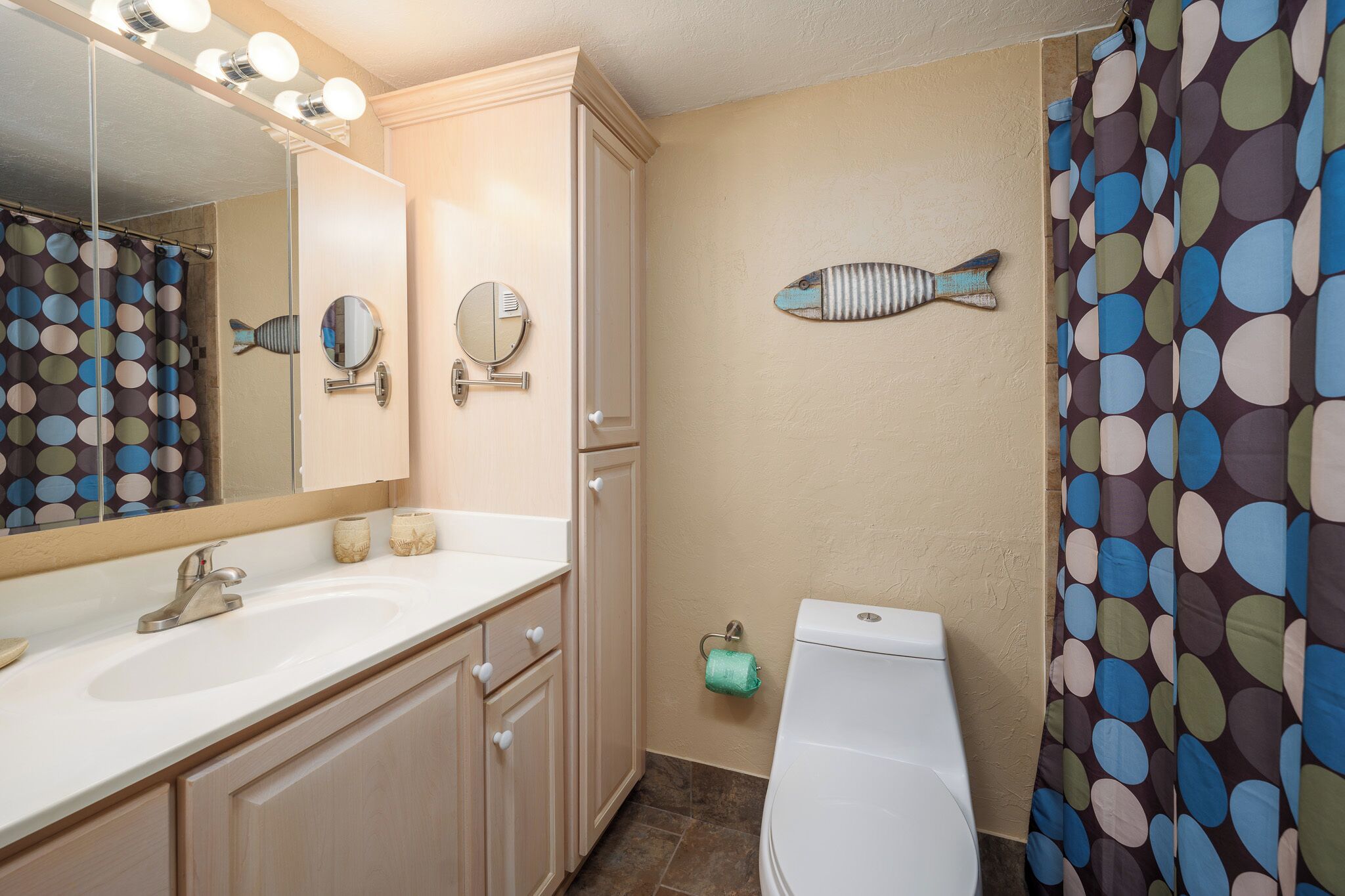 A bathroom with a white sink, two mirrors, a toilet, and a shower curtain with a polka dot pattern.