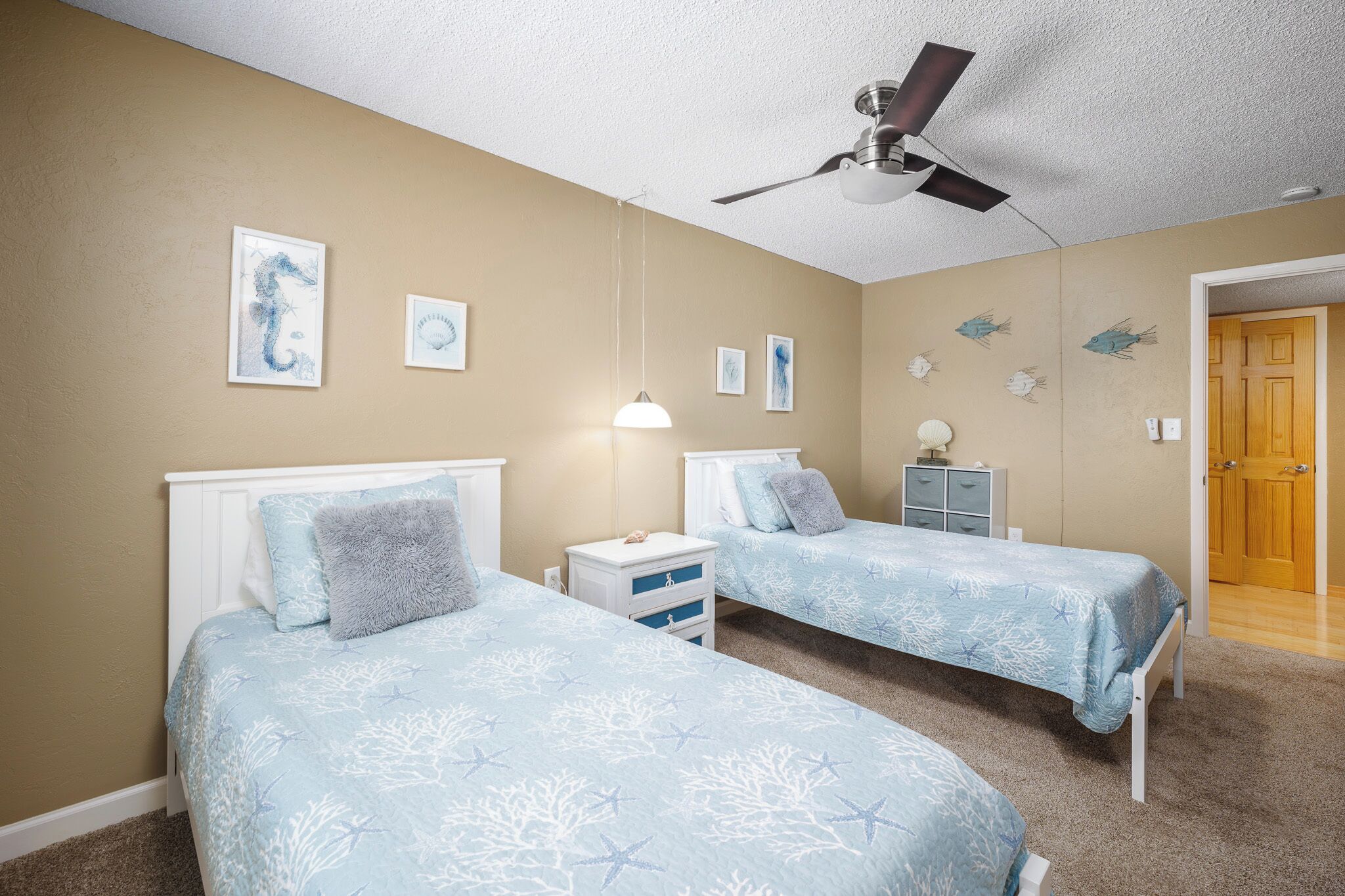 A bedroom with two beds, a ceiling fan, wall art, and a nightstand.
