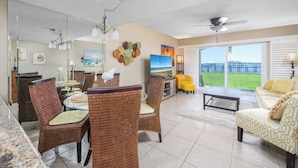 A spacious living area with a dining table, wicker chairs, a sofa, and a view of the outdoors. - Point Matanzas B3 by Distinctive Beach Rentals (St. Augustine)