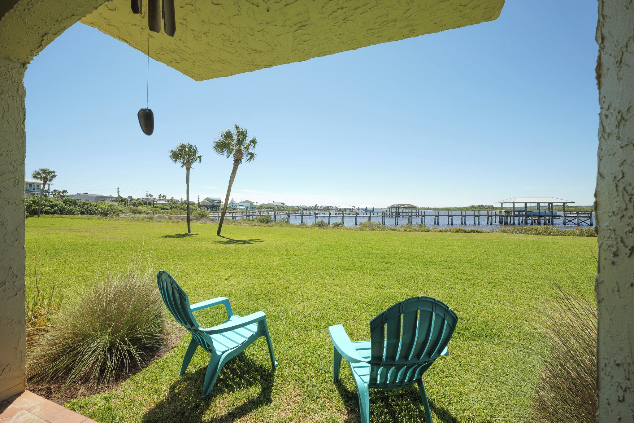 A grassy area with two green chairs and a hanging object, overlooking a body of water and a pier.