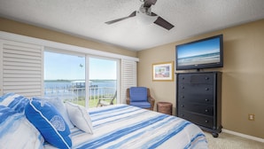 A bedroom with a bed, a dresser, a television, and a view of the ocean. - Point Matanzas B3 by Distinctive Beach Rentals (St. Augustine)