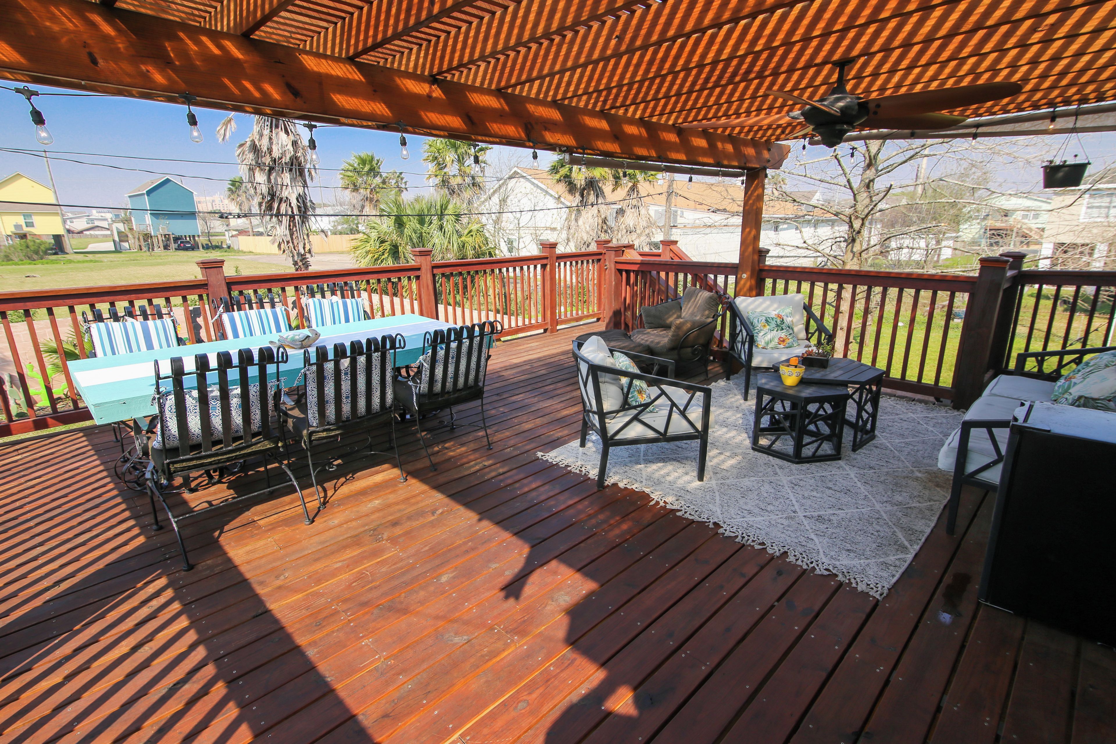 A covered outdoor patio with a wooden deck, a table with chairs, and a seating area with a sofa and a small table.