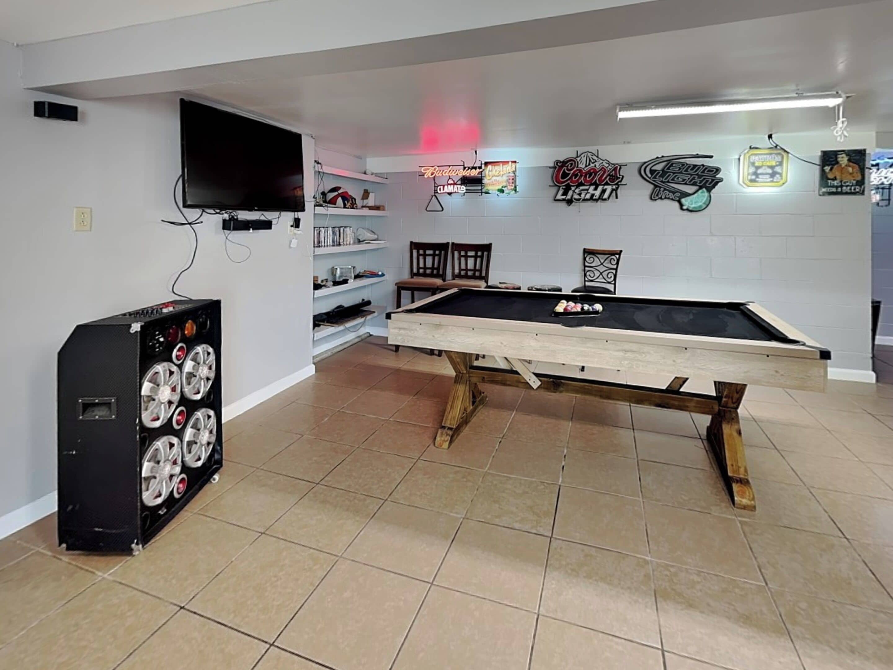 A pool table in a room with a TV, shelves with various items, and neon signs on the wall.
