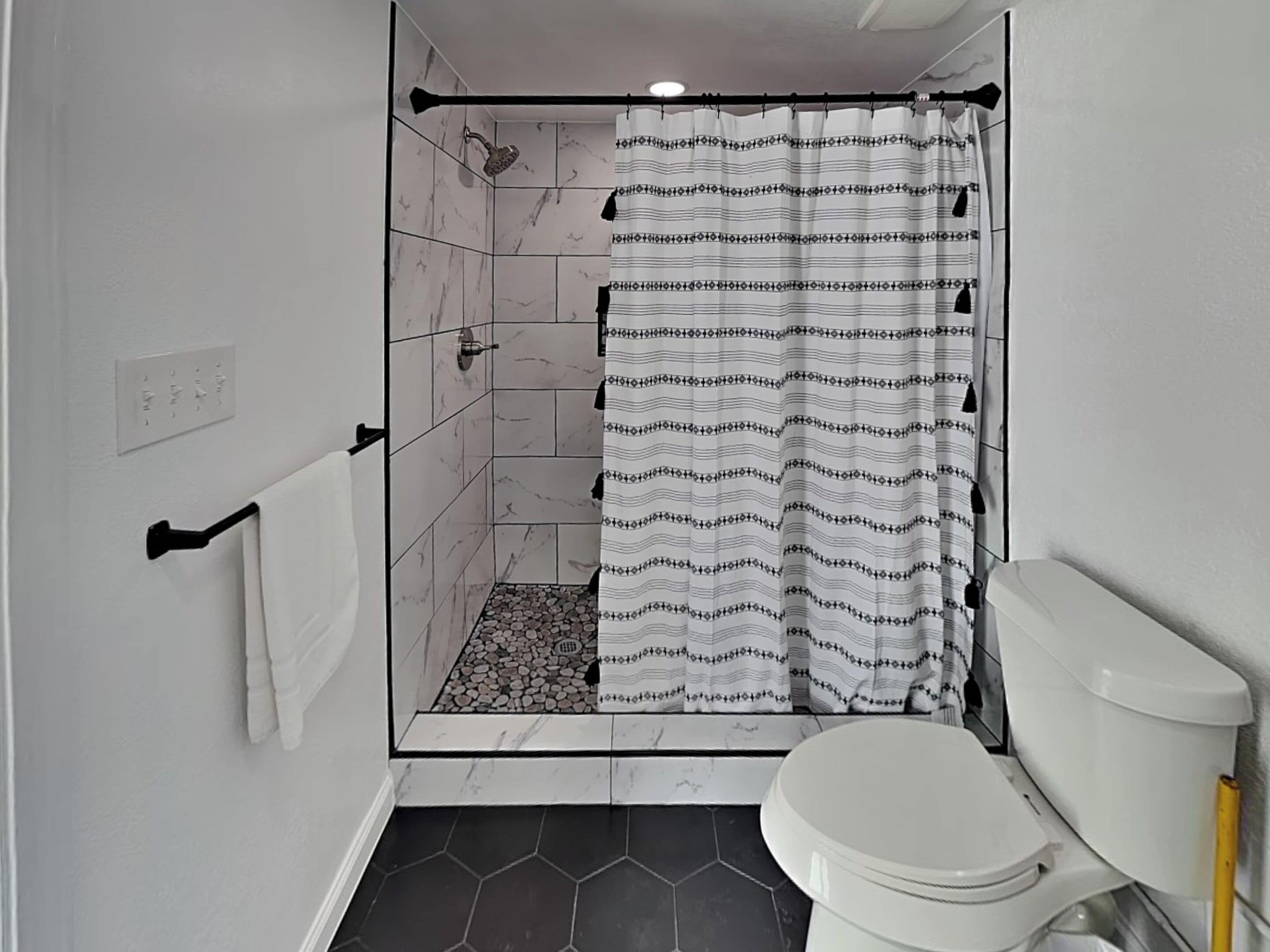 A bathroom with a shower, toilet, and tiled floor.