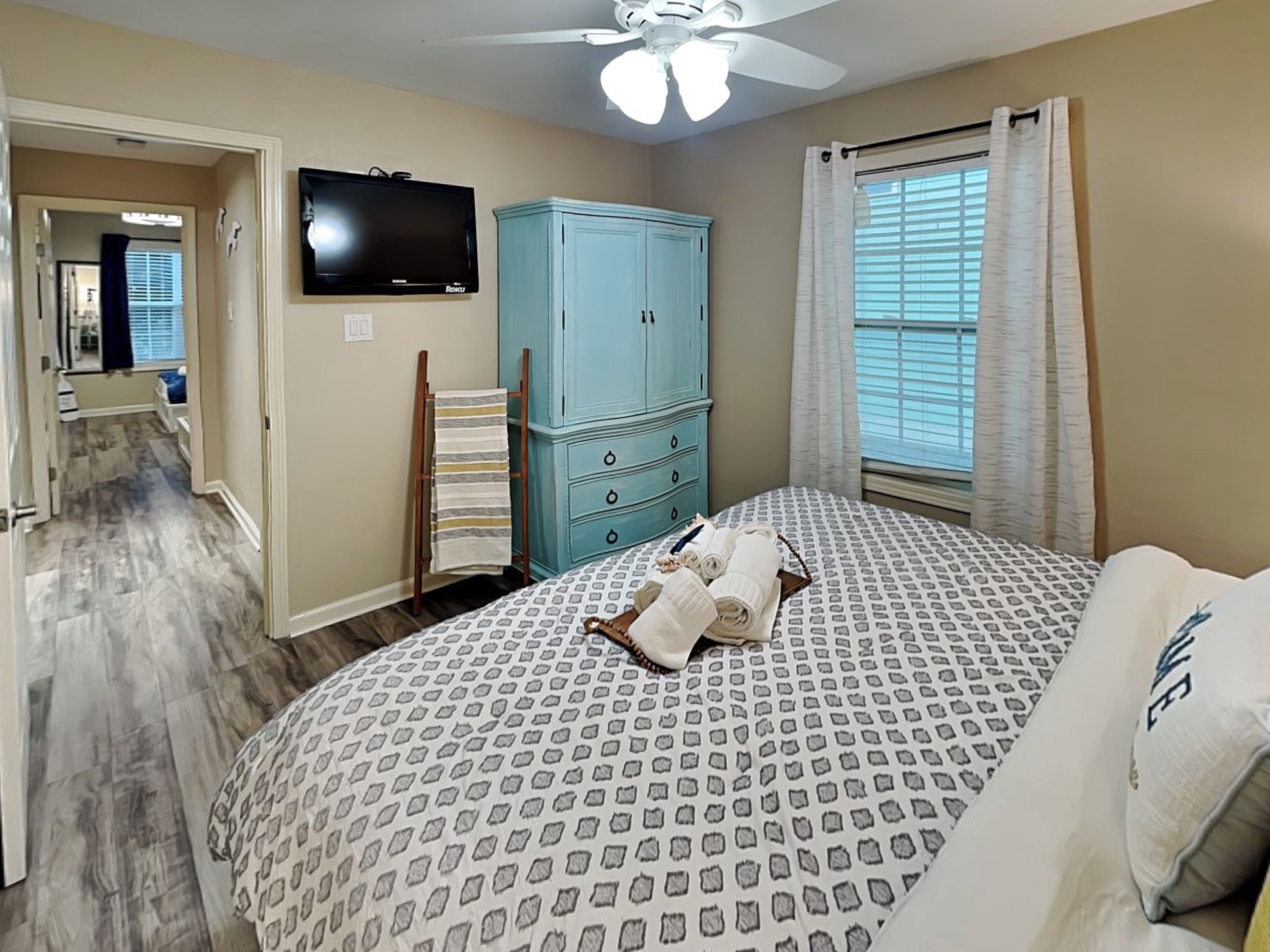 A bedroom with a bed, a ceiling fan, a TV, a wardrobe, and a window with curtains.