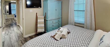 A bedroom with a bed, a ceiling fan, a TV, a wardrobe, and a window with curtains.