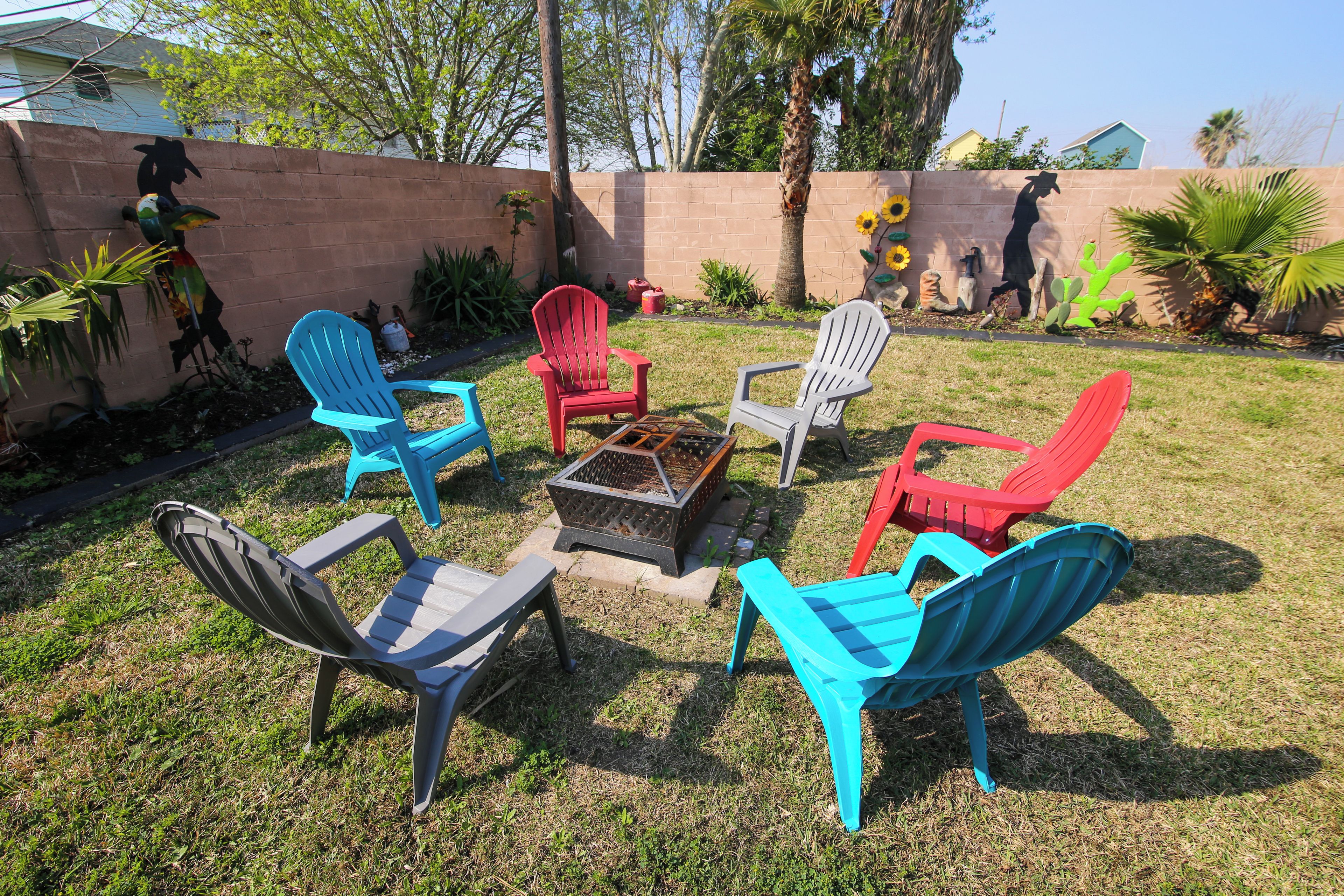 Un giardino sul retro con un braciere circondato da poltrone Adirondack colorate.