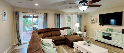 A living room with a sectional sofa, a coffee table, a TV, and a ceiling fan.