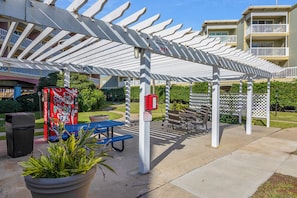 A covered outdoor seating area with a vending machine, trash bin, and potted plants. - Relax by the Beach by Ryson Vacation Rentals (Galveston)