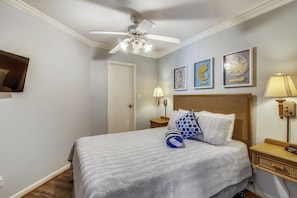 Ein ordentlich eingerichtetes Schlafzimmer mit Bett, Deckenventilator, Nachttisch und Wandbildern.