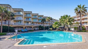 A swimming pool surrounded by a multi-story hotel with balconies and palm trees. - Relax by the Beach by Ryson Vacation Rentals (Galveston)