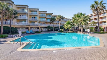 Ein Schwimmbecken, umgeben von einem mehrstöckigen Hotel mit Balkonen und Palmen.