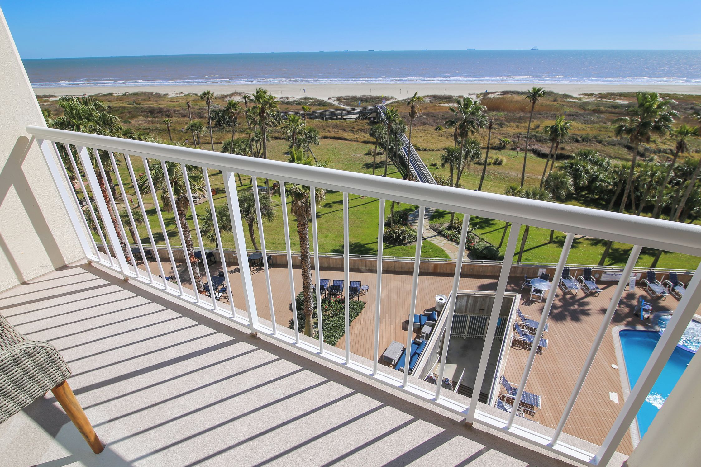 Un balcón con vistas al océano, un área de piscina y mobiliario exterior.