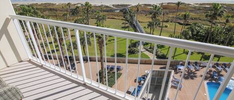 Un balcón con vistas al océano, un área de piscina y mobiliario exterior.