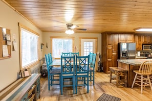 A wooden-paneled kitchen with a central island, a ceiling fan, and a dining area with blue chairs.