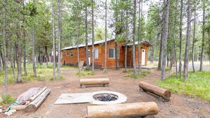 A rustic cabin surrounded by tall trees, with a fire pit and logs in the foreground. - Le Chalet at Mack's Inn CLOSE TO YELLOWSTONE 里黄石公园很近；我说中文！ (Island Park)