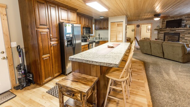 A spacious kitchen with wooden cabinets, a granite countertop, and a built-in island with bar stools. - Le Chalet at Mack's Inn CLOSE TO YELLOWSTONE 里黄石公园很近；我说中文！ (Island Park)