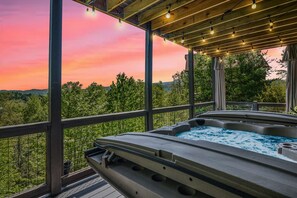 Boblebad med træterrasse og udsigt til en solnedgang over et skovlandskab.