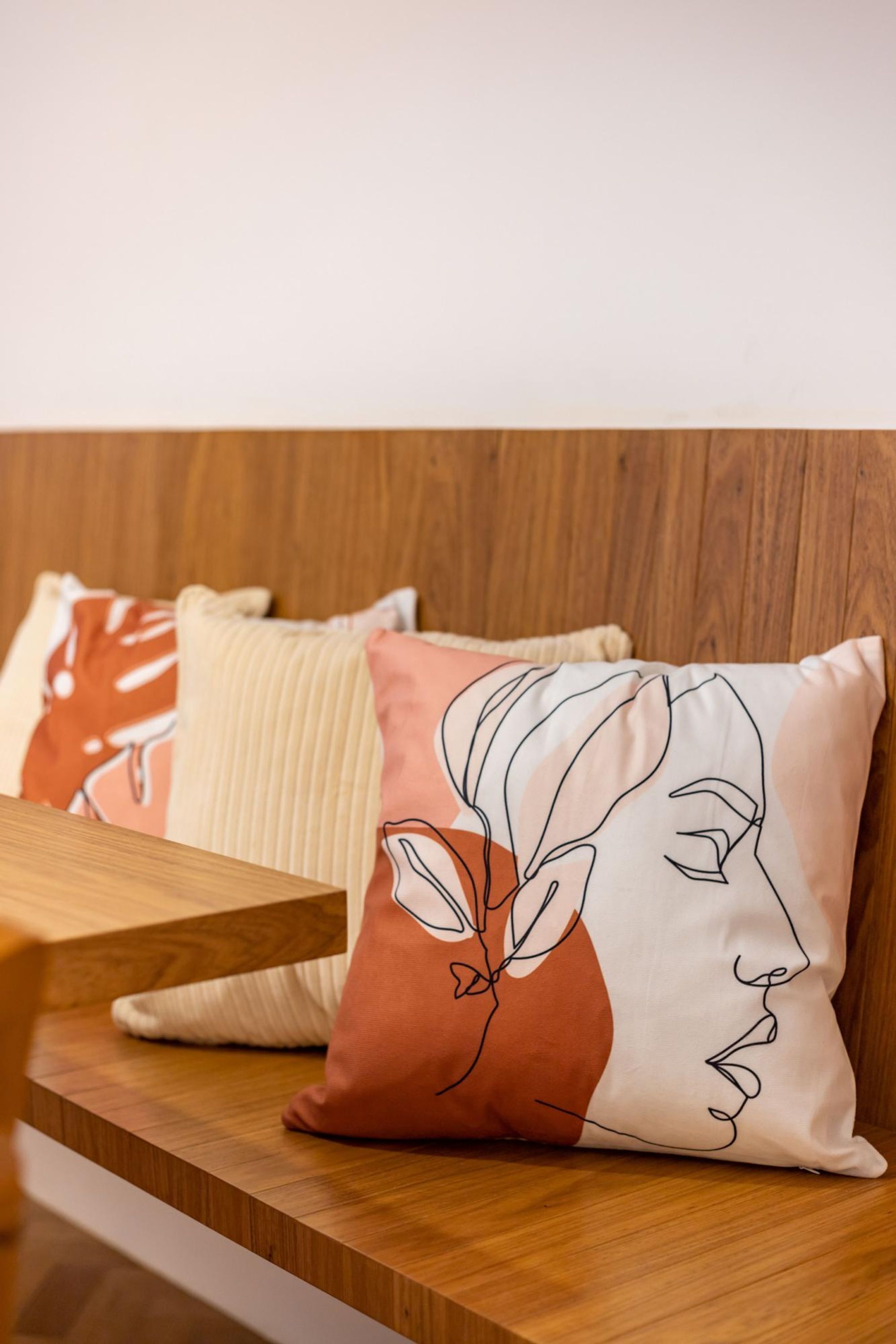 Un banc en bois avec un coussin orné d’un dessin linéaire représentant un visage.