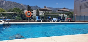 Ein Swimmingpool mit Liegestühlen und Sonnenschirmen, einem Rettungsring und Blick auf Berge.