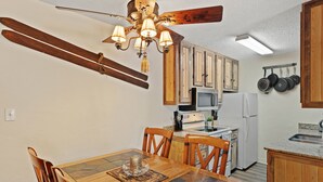 Un comedor con una mesa y sillas de madera, una araña y una cocina al fondo.
