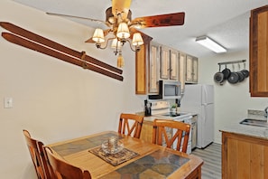 Ein Essbereich mit Holztisch und -stühlen, einer Chandelierleuchtre und einer Küche im Hintergrund.
