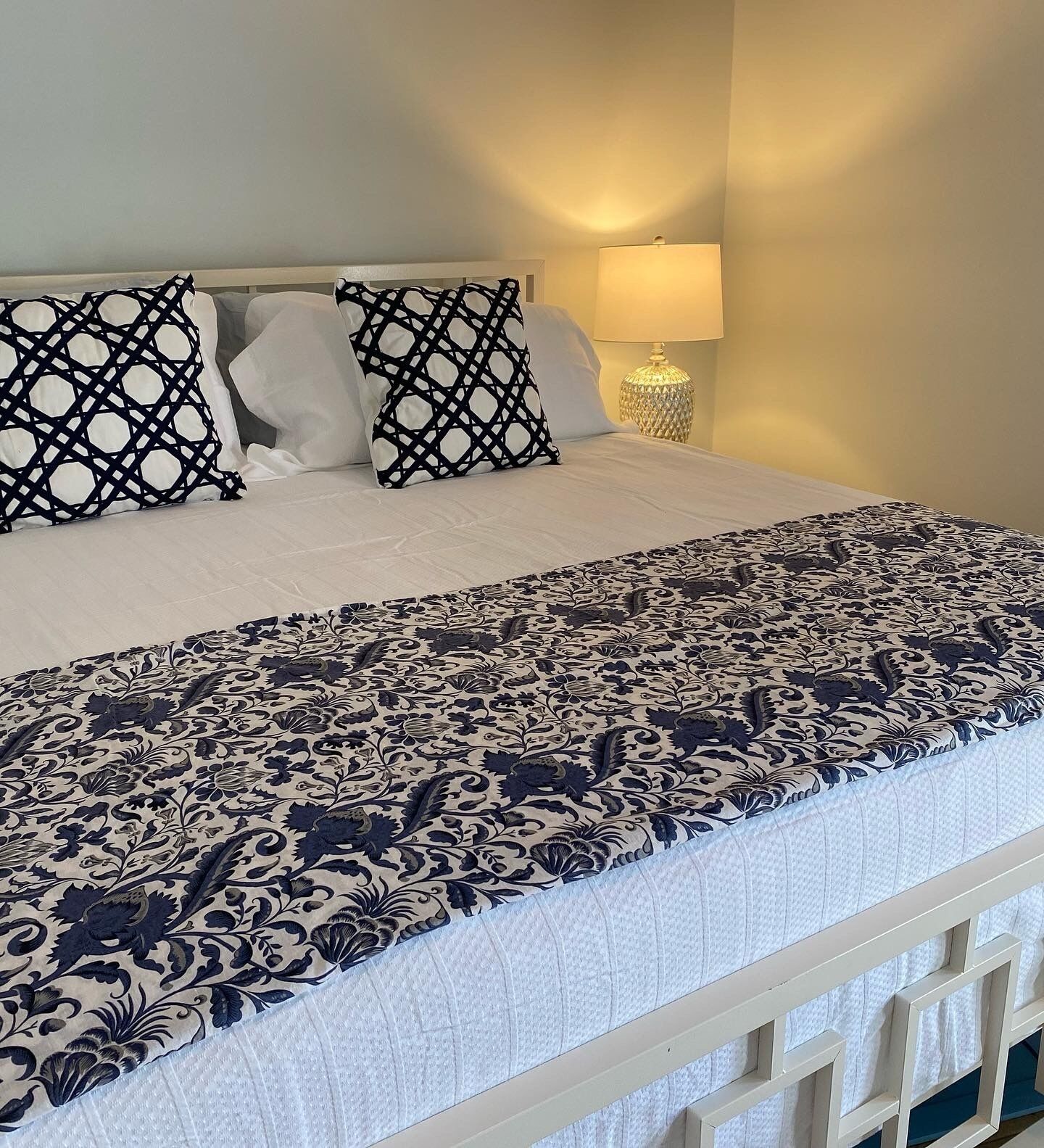 Een net opgemaakt bed met een beddekleed met dessin en twee decoratieve kussens.