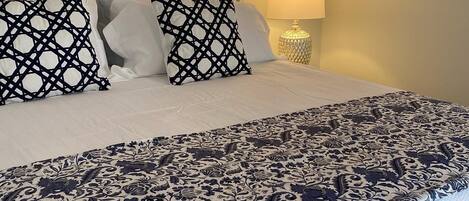 Een net opgemaakt bed met een beddekleed met dessin en twee decoratieve kussens.