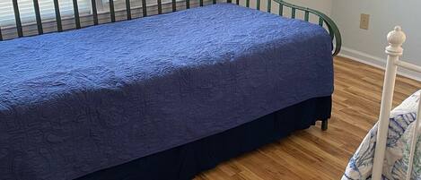 Una habitación con cama, suelo de madera y ventana con persianas.