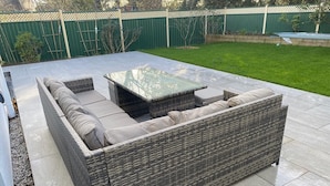 A wicker sofa with cushions and a glass-top coffee table in an outdoor patio area. - Sleeps8- Ecofriendly- Kingbeds- Familyfriendly (Wadebridge)