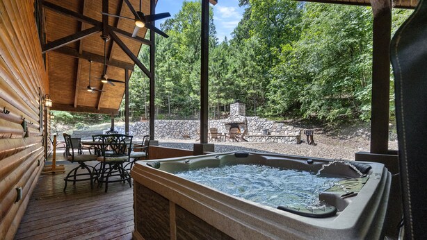 A wooden deck with a hot tub, outdoor seating, and a stone fireplace. - PRIVATE Peaceful Cabin on 1.5 Acres with Hot Tub, Deck & HUGE Outdoor Fireplace! (Broken Bow)