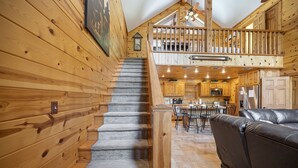 A wooden interior with a staircase leading to a loft area, a kitchen with modern appliances, and a leather sofa in the living area. - PRIVATE Peaceful Cabin on 1.5 Acres with Hot Tub, Deck & HUGE Outdoor Fireplace! (Broken Bow)