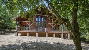 A wooden cabin with a balcony, surrounded by trees and gravel. - PRIVATE Peaceful Cabin on 1.5 Acres with Hot Tub, Deck & HUGE Outdoor Fireplace! (Broken Bow)