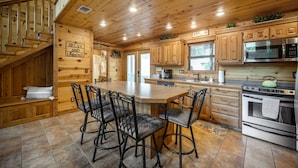 A wooden cabin-style kitchen with a central island, bar stools, and a stove. - PRIVATE Peaceful Cabin on 1.5 Acres with Hot Tub, Deck & HUGE Outdoor Fireplace! (Broken Bow)