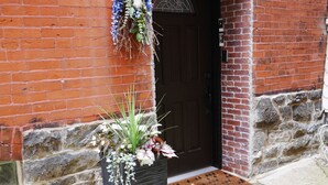 A brick building with a 'WELCOME' sign above the door, a wreath, and a planter with flowers. - Cozy 2 bdrm Unit/Big Kitchen-2 TV- University City (Philadelphia)