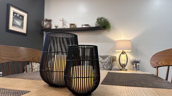 Two black cylindrical vases with vertical slits on a wooden table, a lamp, and a framed picture on the wall.